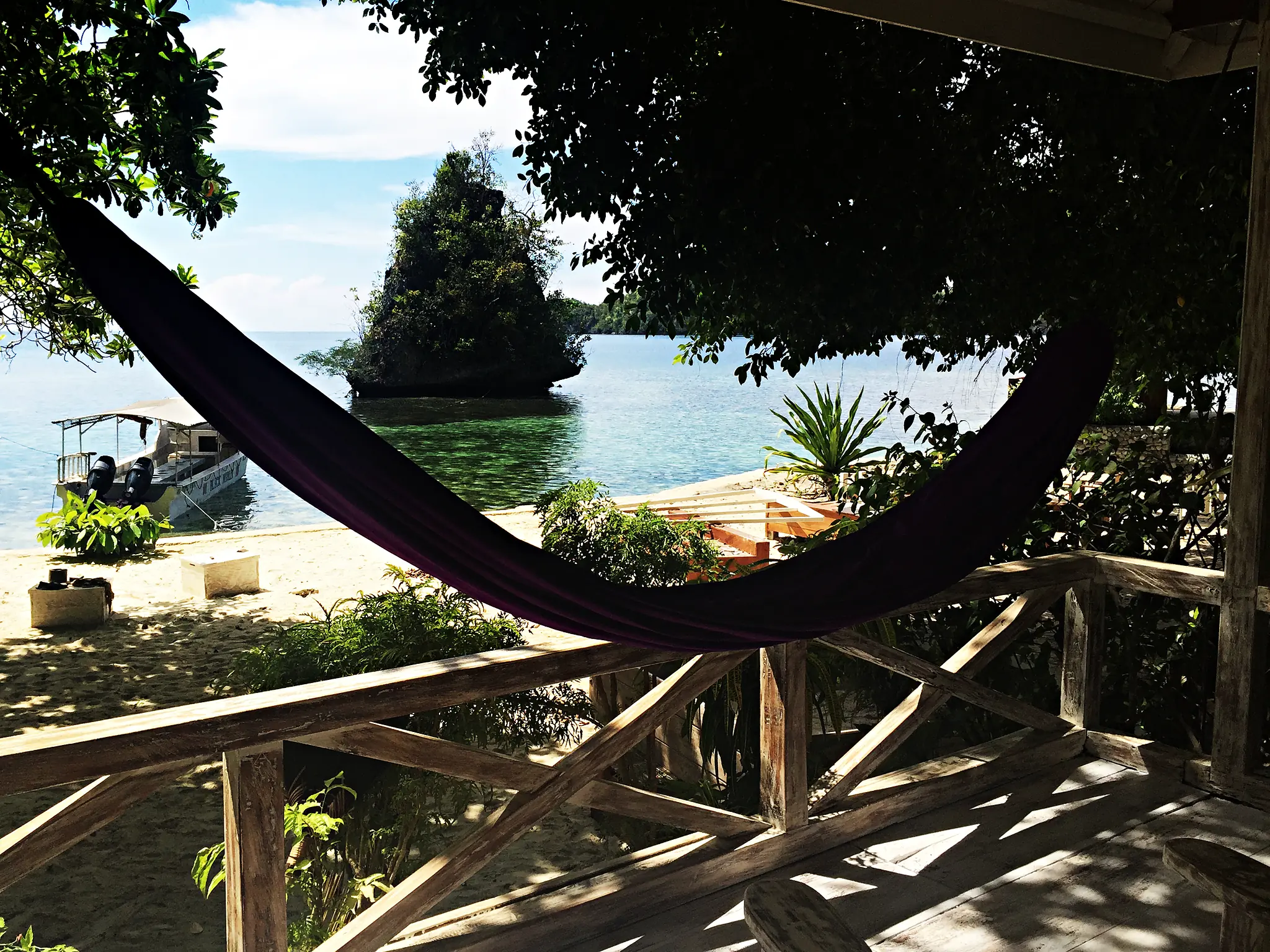 a purple hammock on the standard bungalow veranda framing the beach, a dive boat and a karst islet