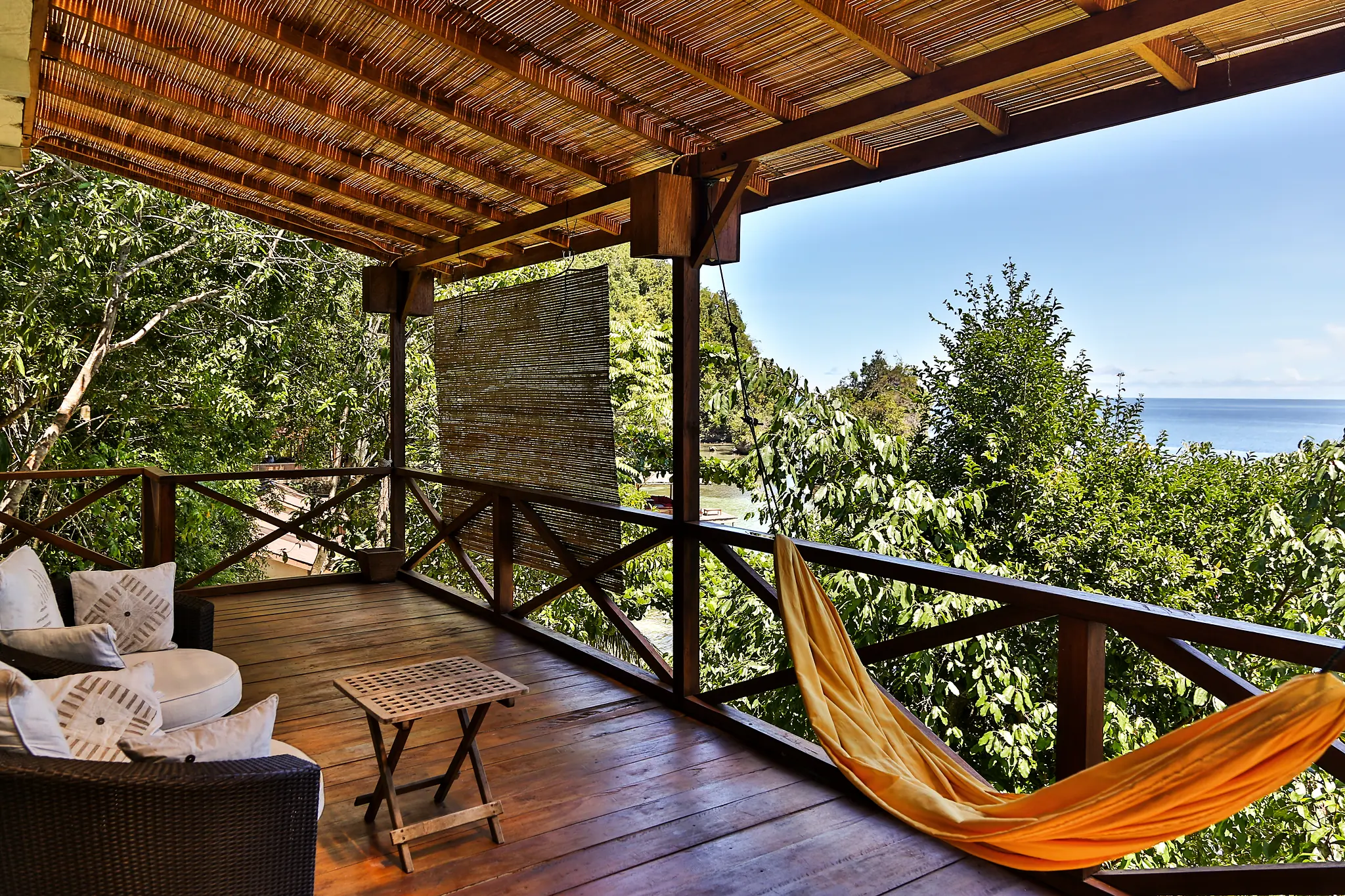 the Cliffside Villa balcony with a hammock and rattan seating above the forest, the sea beyond